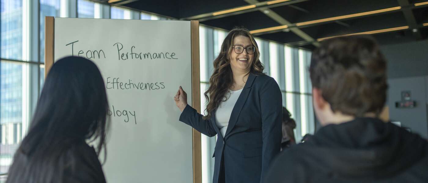 A student wearing a sports jacket stands infront of a small group during a presentation